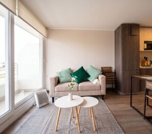 A modern living room with a beige sofa, two white round tables, and a view of the outdoors through large windows.