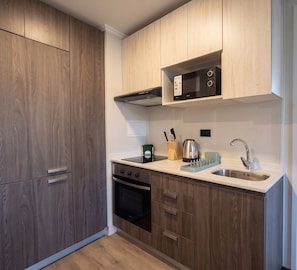Eine kompakte Küche mit Holzschränken, einer eingebauten Mikrowelle, einem Edelstahl-Spülbecken und einem schwarzen Backofen.