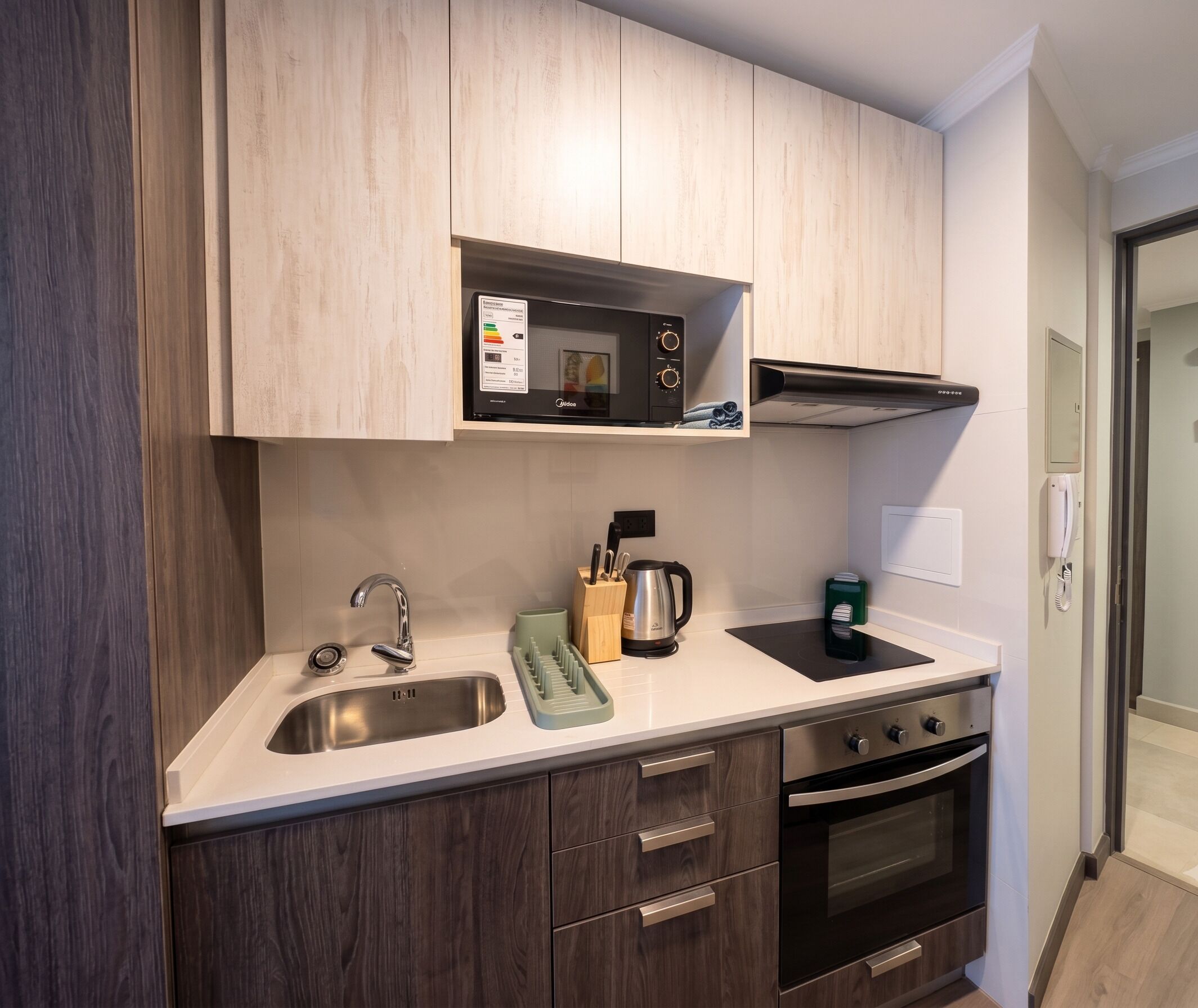 A modern kitchen with a stainless steel sink, a microwave, a kettle, and an oven.