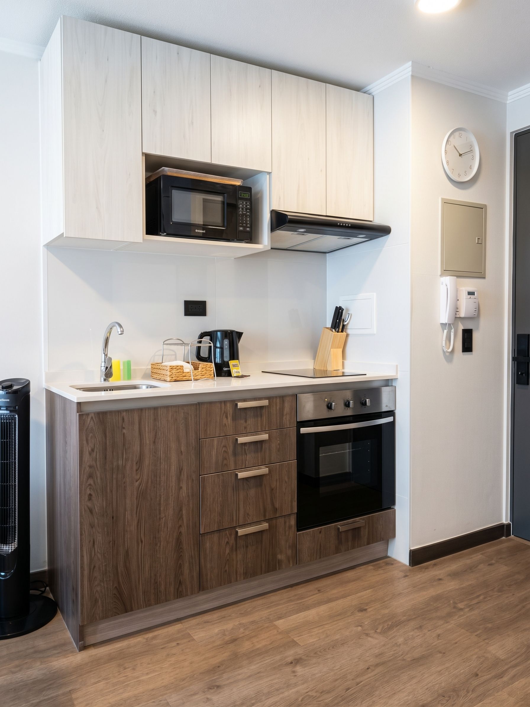 A modern kitchen with wooden cabinets, a built-in microwave, a kettle, and a coffee maker.