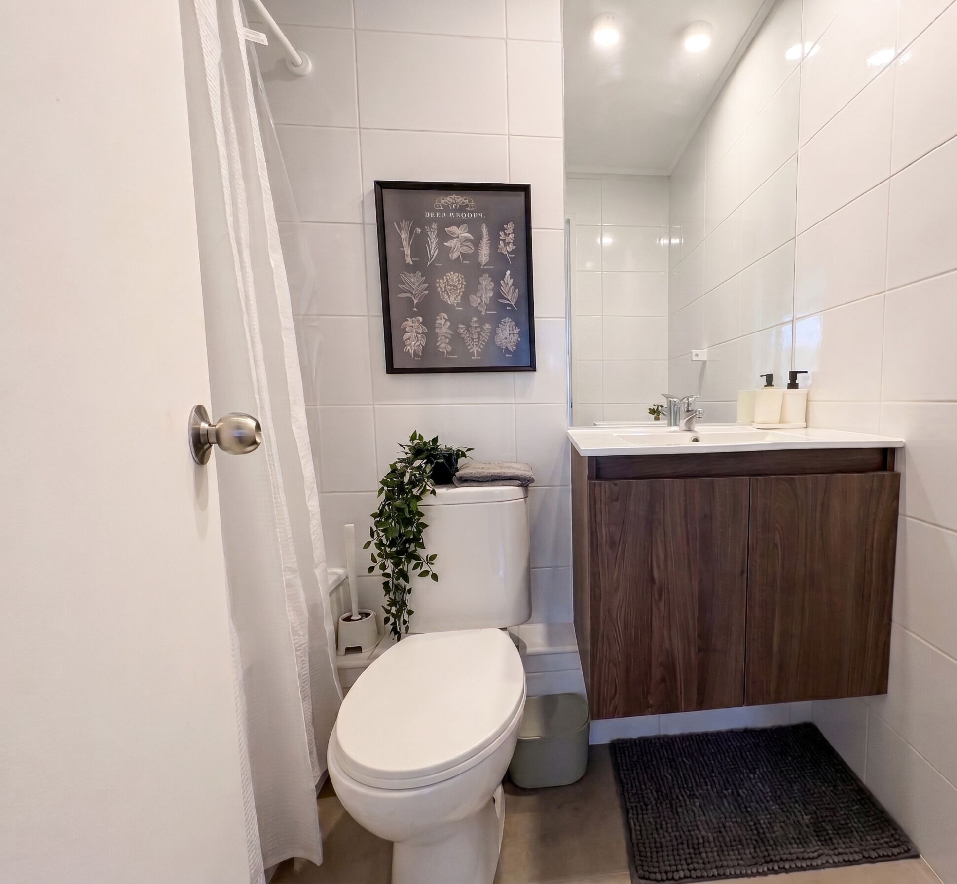 Een moderne badkamer met toilet, wastafel en een ingelijste botanische illustratie aan de muur.