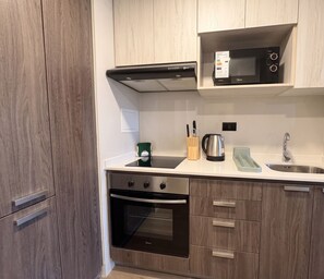 A modern kitchen with wooden cabinets, a stainless steel oven, a microwave, and a sink.