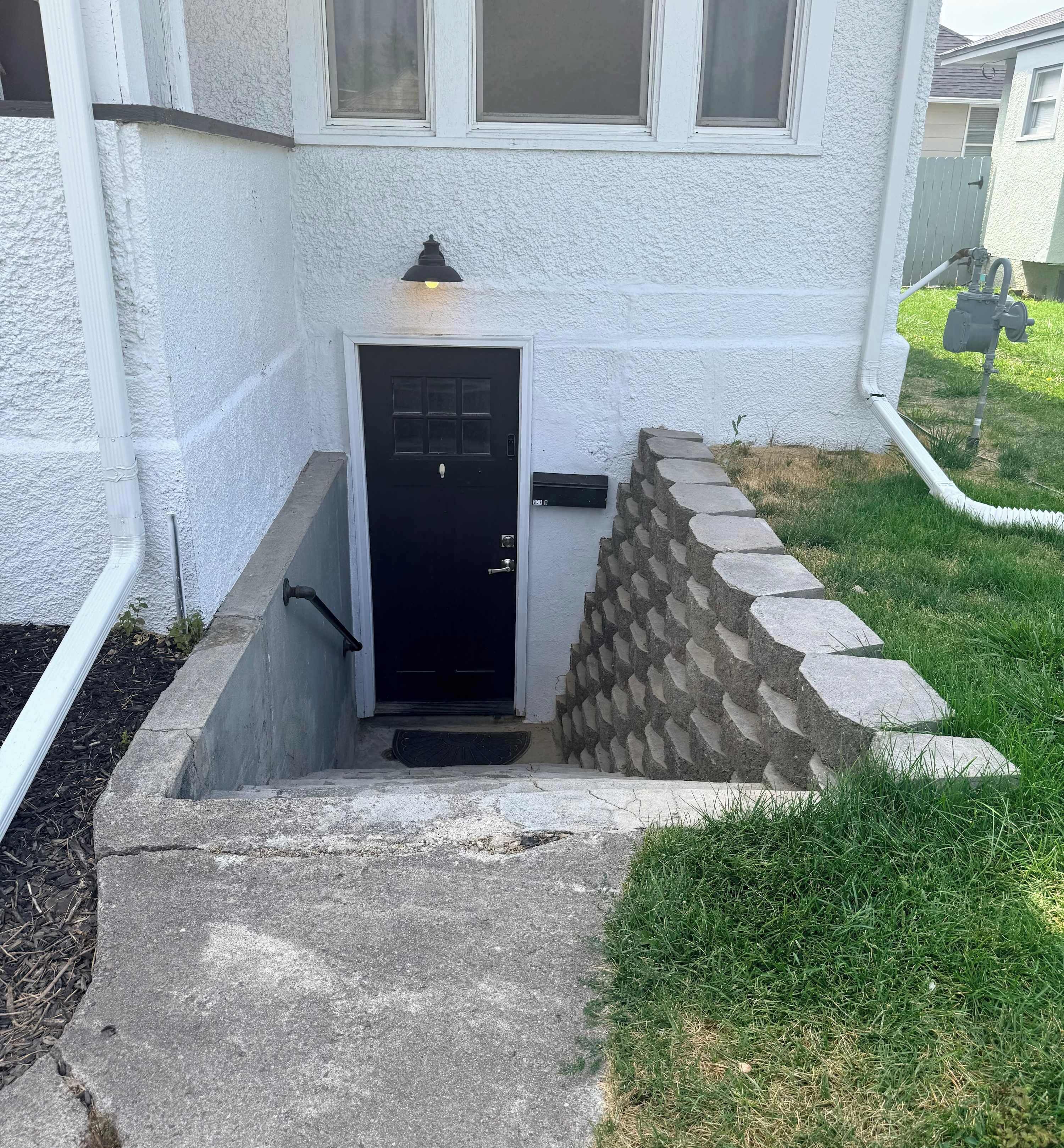 Ein Haus mit einer schwarzen Tür, einem Betontritt vor dem Eingang und einer Steinmauer.