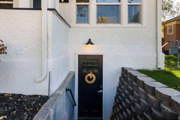 Una casa con puerta principal negra, un accesorio de iluminación encima de la puerta y un muro de piedra a la derecha.