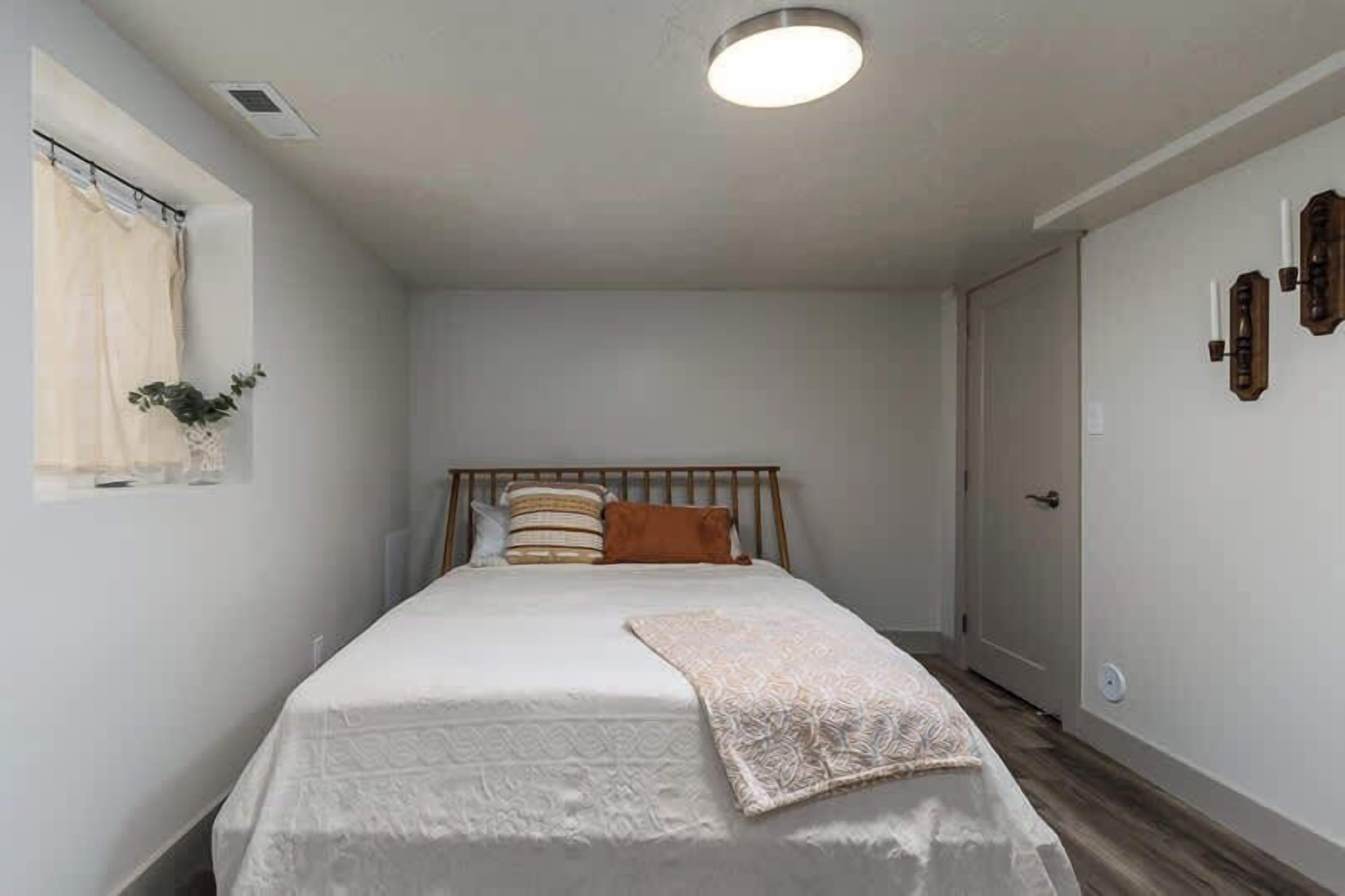 A bedroom with a single bed, a window with curtains, a bedside table, and a door.