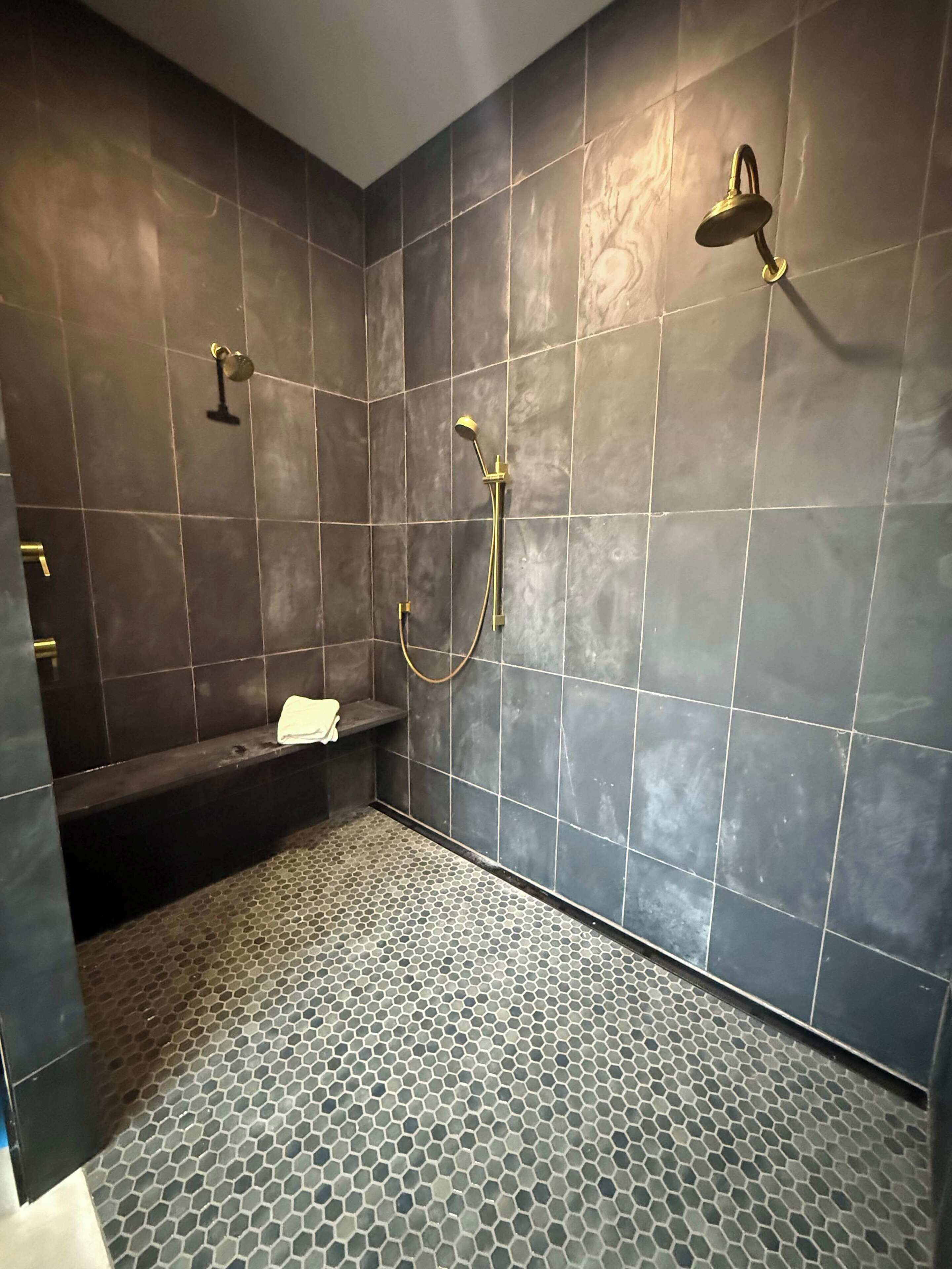 A modern bathroom with dark tiles, a hexagonal patterned floor, a bathtub, and a shower with a handheld showerhead.