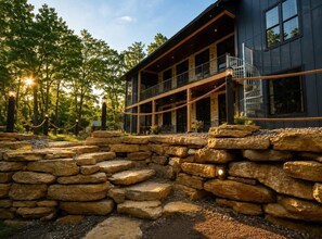 A modern building with a stone retaining wall, a balcony, and a view of trees. - The Shipwreck Shack • Castle Rock Lake • Sleeps 18 (Mauston)