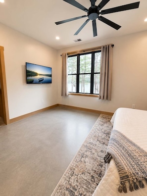 A bedroom with a bed, a ceiling fan, a large window with curtains, and a wall-mounted TV. - The Shipwreck Shack • Castle Rock Lake • Sleeps 18 (Mauston)