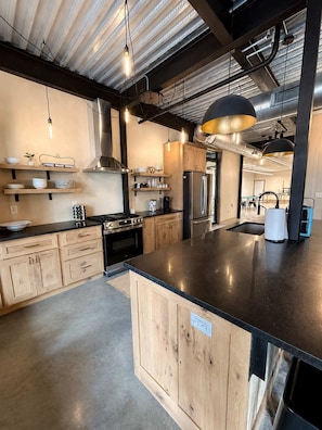 Une cuisine moderne avec des meubles en bois, des appareils en acier inoxydable et des luminaires suspendus.