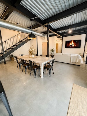 Une pièce spacieuse comprenant une table à manger, des chaises, un canapé et un téléviseur diffusant une image de cheminée.