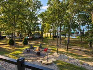 A campsite with a fire pit, chairs, and a view of a lake. - The Shipwreck Shack - Fall Getaway | Hot Tub • Sleeps 18 (Mauston)