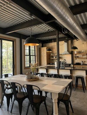 A modern kitchen with a large island, pendant lighting, and a dining area with a table and chairs. - The Shipwreck Shack - Fall Getaway | Hot Tub • Sleeps 18 (Mauston)