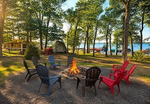 A campsite with a fire pit surrounded by chairs, a tent, and a lake view. - The Shipwreck Shack • Castle Rock Lake • Sleeps 18 (Mauston)
