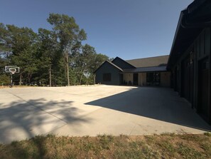 A building with a covered parking area and a basketball hoop. - The Shipwreck Shack - Fall Getaway | Hot Tub • Sleeps 18 (Mauston)