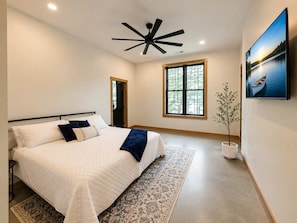 Une chambre à coucher avec un lit, un ventilateur de plafond, une fenêtre et un tableau.