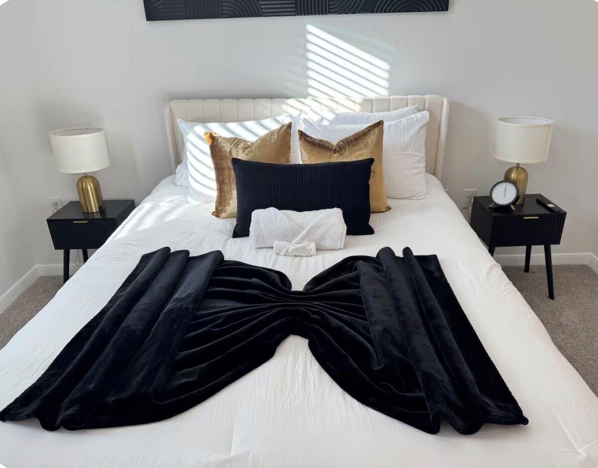 Una cama bien hecha con una manta negra, ropa de cama blanca y almohadas decorativas.