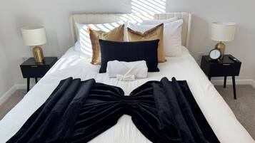 Una cama bien hecha con una manta negra, ropa de cama blanca y almohadas decorativas.
