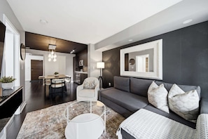A modern living room with a grey sofa, a coffee table, and a dining area with a chandelier. - DT Gem near the CN Tower & Rogers Centre! (Toronto)