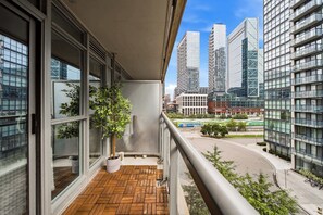 A balcony with a potted plant, large windows, and a view of modern buildings. - DT Gem near the CN Tower & Rogers Centre! (Toronto)