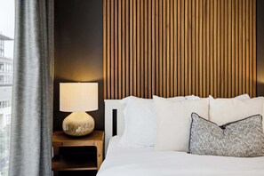 Ein Hotelzimmer mit Bett, Nachttisch mit Lampe und Blick auf die Stadt durch ein Fenster.