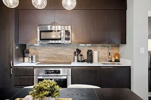A modern kitchen with dark cabinetry, a stainless steel microwave, a coffee maker, and a built-in oven. - DT Gem near the CN Tower & Rogers Centre! (Toronto)