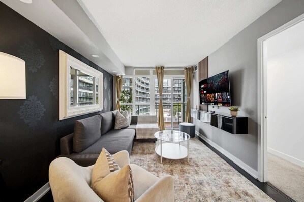 A modern living room with a sofa, a coffee table, and a flat-screen TV mounted on the wall. - DT Gem near the CN Tower & Rogers Centre! (Toronto)