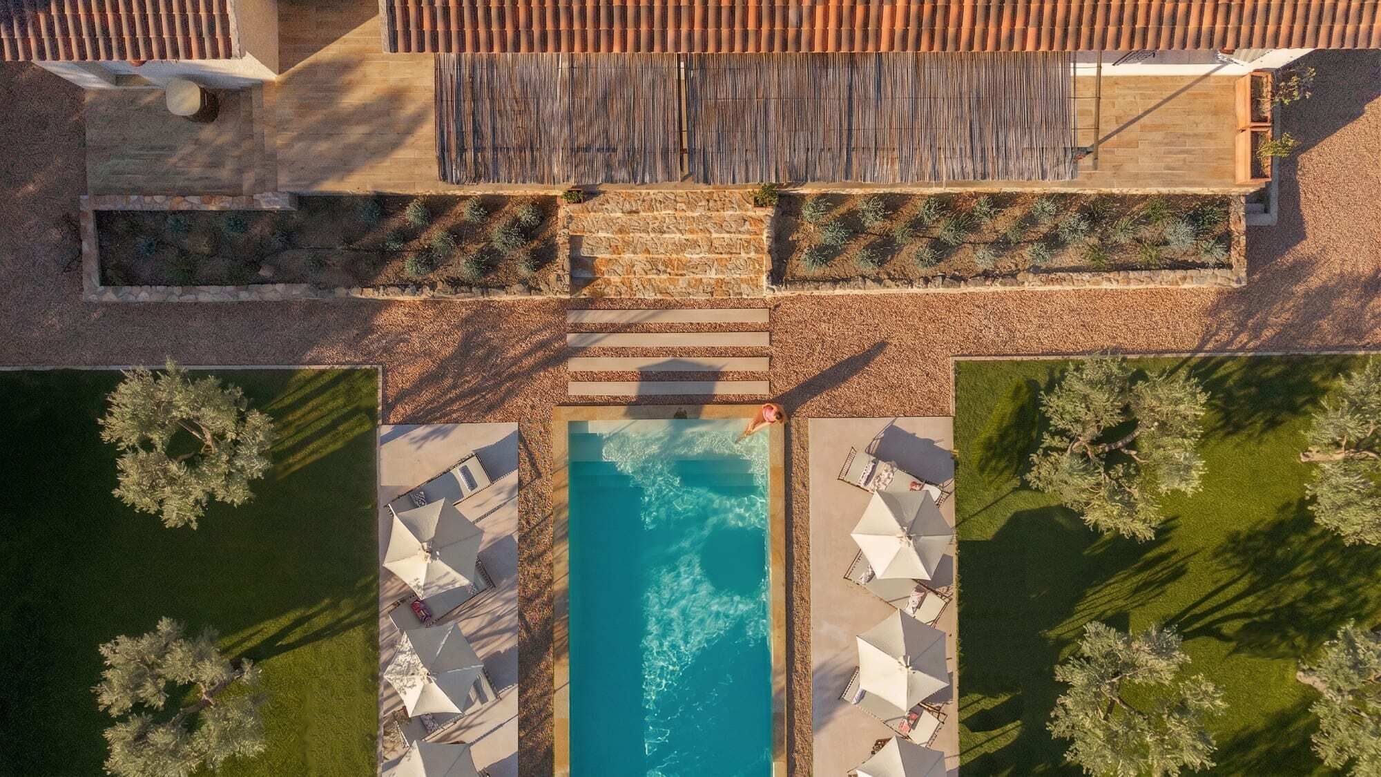 Vue aérienne d’un espace piscine avec un chemin de pierre menant à la piscine, entouré de verdure et ombragé par des arbres.
