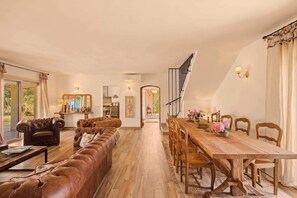 Ein geräumiges Wohnzimmer mit einem langen, braunen Ledersofa, einem Holzespeisetisch mit Stühlen und einer Treppe, die zu einer oberen Ebene führt.