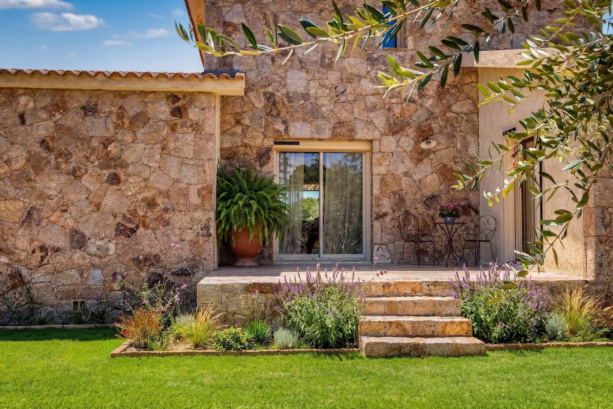 Une maison en pierre avec une grande plante en pot, un petit patio avec une table et des chaises, et une pelouse bien entretenue.