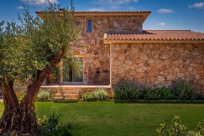 A stone building with a tiled roof, a small window, and a door. There is a tree in the foreground and a well-maintained lawn. - Ô · Ô1 L'Aube Collection — 5-bedroom villa with private pool, Lecci, Southern Corsica (San-Gavino-di-Carbini)