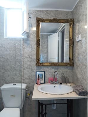 Un bany amb paret de marbre, mirall amb marc daurat, un lavabo blanc, un vàter i una fotografia emmarcada.
