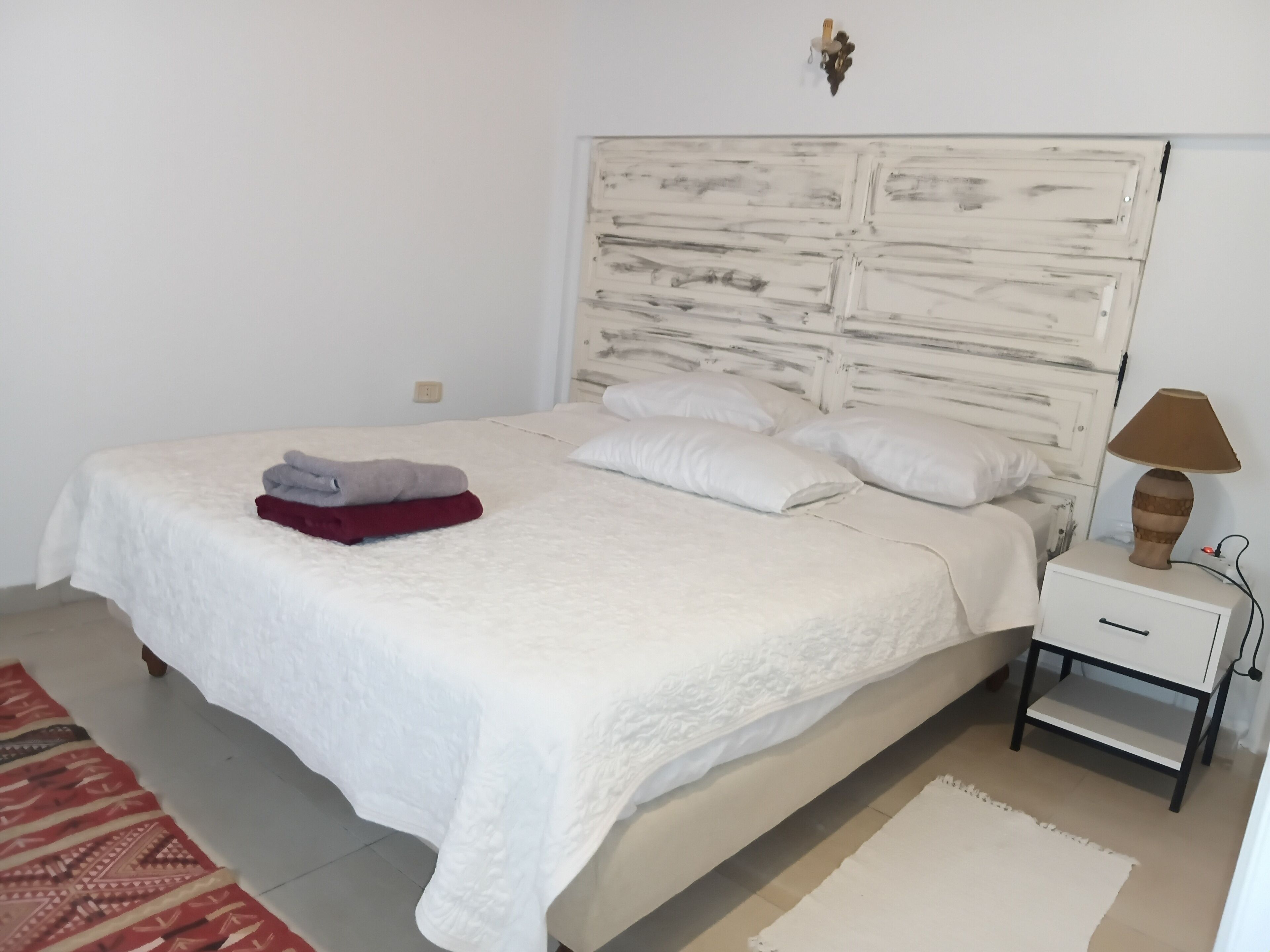 Een net opgemaakt bed met een witte dekbedovertrek, twee kussens en een gevouwen rode en grijze deken aan de zijkant.