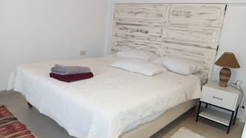 Een net opgemaakt bed met een witte dekbedovertrek, twee kussens en een gevouwen rode en grijze deken aan de zijkant.