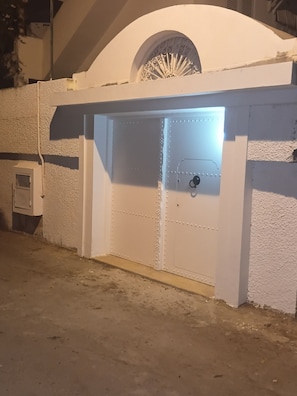 Una entrada blanca en arc amb una reixa metàl·lica, un teclat de codi de seguretat i un petit objecte rectangular blanc adossat a la paret a l'esquerra.
