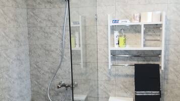 Een douchecabine met glazen wanden, een handdouche, een handdoekrek en een plank met toiletartikelen.