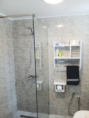 A glass-enclosed shower with a handheld showerhead, a towel rack, and a shelf with toiletries. - Vrbo Property (tunis)