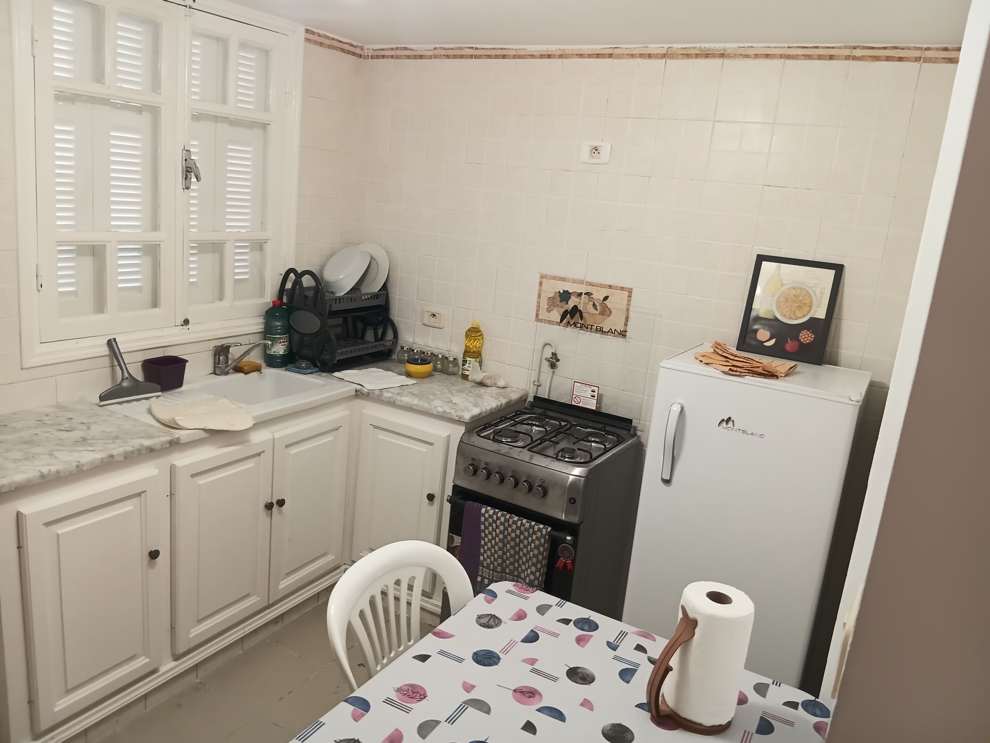 Eine Küche mit weißen Schränken, einem Gaskochfeld, einer Spüle und einem Kühlschrank.