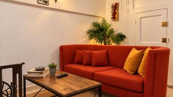 Ein Wohnzimmer mit einem roten Sofa, einem Holztisch, einer Topfpflanze und Wandbildern.