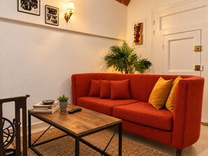 A living room with a red sofa, a wooden coffee table, a potted plant, and wall-mounted artwork. - Patio Secret Private Studio in Sidi Bou Saïd—Pets Allowed (tunis)