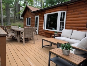 A wooden cabin with a deck, furnished with a sofa, tables, and chairs. - Cozy cabin on All Sports Lake with private beach! Close to ski resorts & trails (Atlanta)