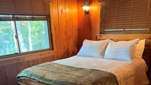 A wooden cabin bedroom with a bed, nightstands, and a window. - Cozy cabin on All Sports Lake with private beach! Close to ski resorts & trails (Atlanta)