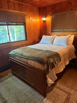 A wooden cabin bedroom with a bed, nightstands, and a window. - Cozy cabin on All Sports Lake with private beach! Close to ski resorts & trails (Atlanta)