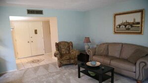 Un salon avec un canapé, un fauteuil, une table basse et un tableau encadré au mur.
