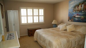 Une chambre à coucher avec un lit, une table de chevet, une commode, une fenêtre et un tableau au mur.
