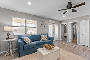 Ein Wohnzimmer mit blauem Sofa, einem kleinen runden Tisch und einem Deckenventilator.