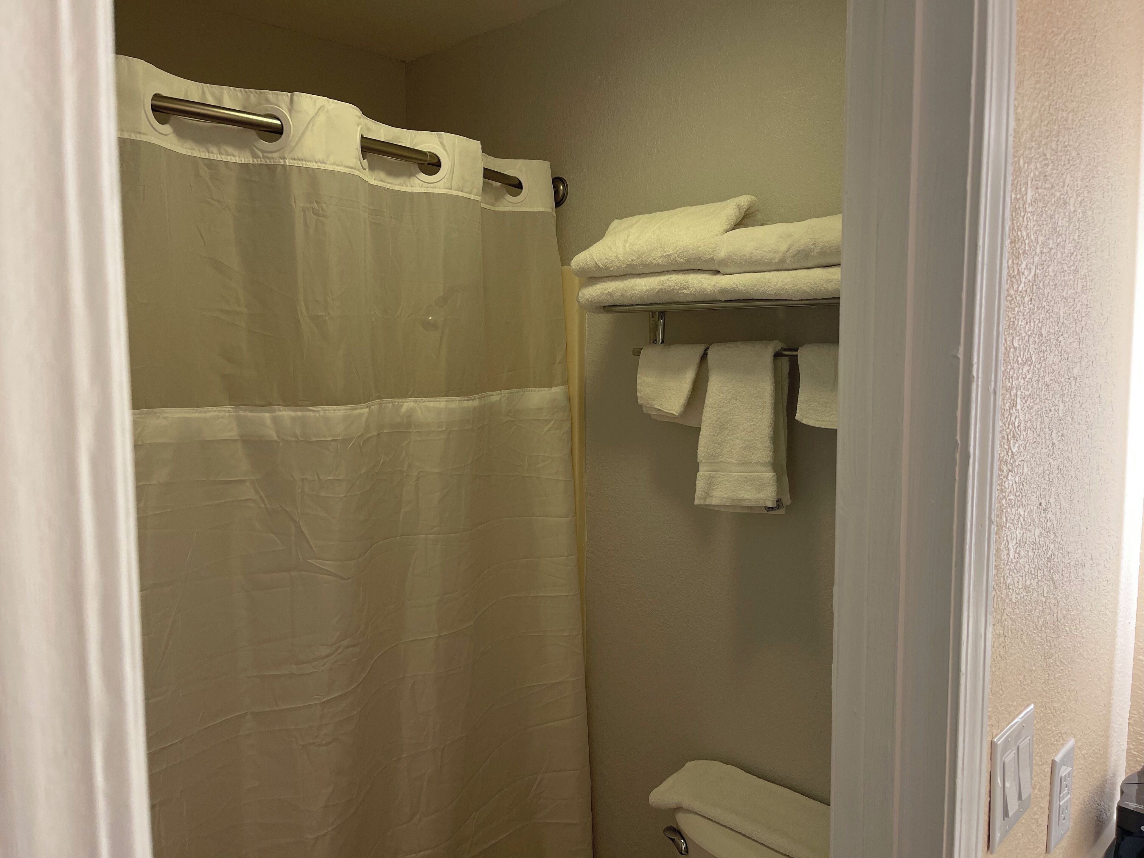 A bathroom with a shower curtain, a towel rack with towels, and a toilet.