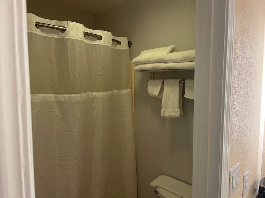 Uma casa de banho com cortina de chuveiro, um porta-toalhas com toalhas e uma sanita.