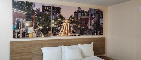 A hotel room with a large cityscape painting on the wall, a wooden headboard, and a bed with white bedding.