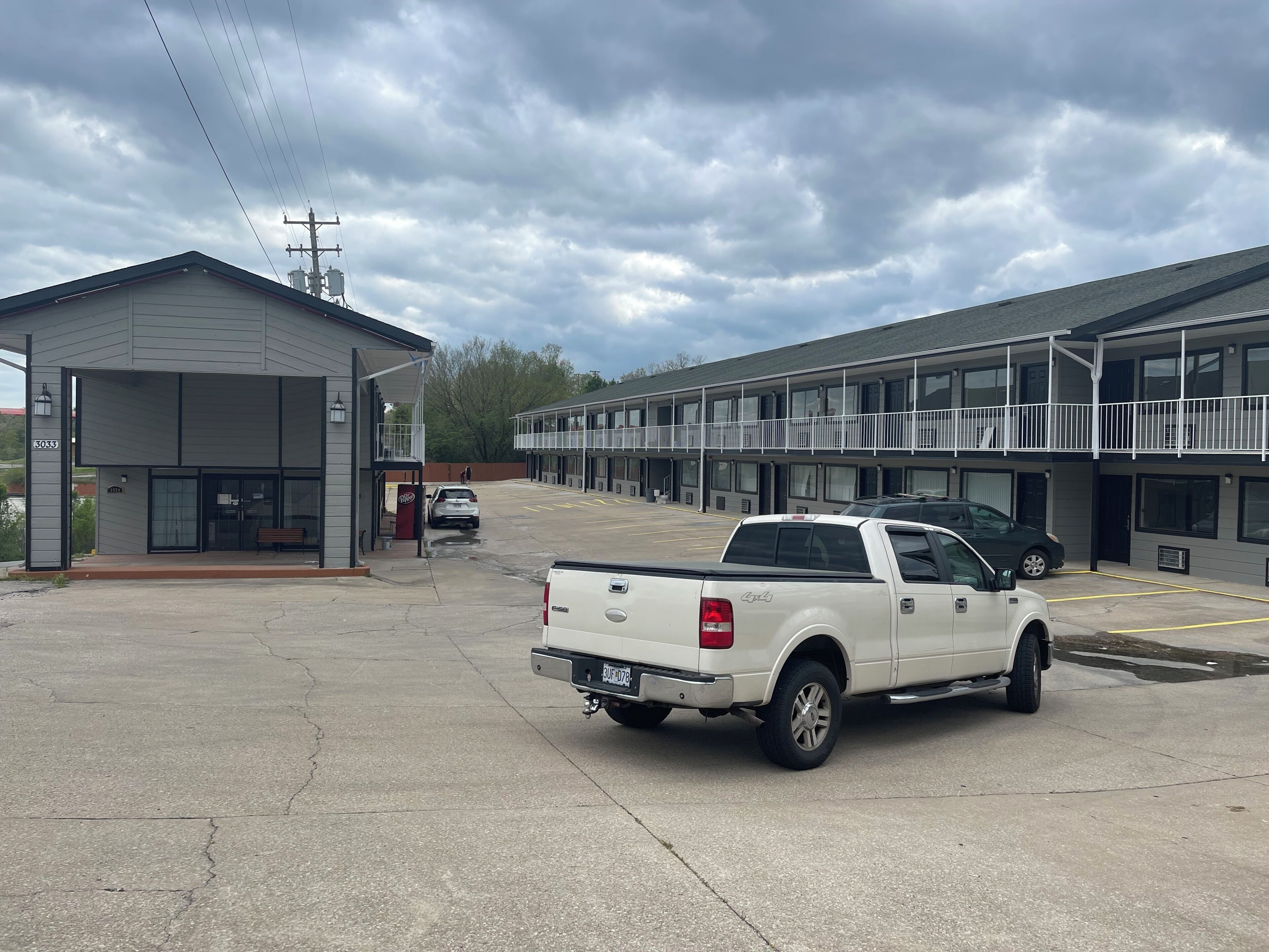 A parking lot with a white pickup truck, a building with a balcony, and a sign with the number 3033.