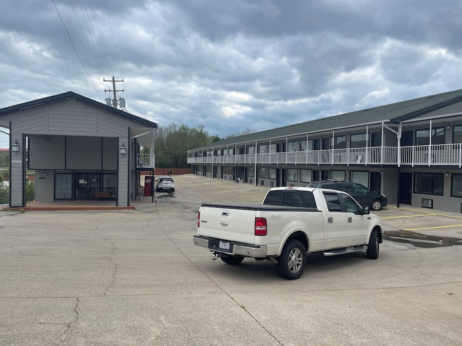 A parking lot with a white pickup truck, a building with a balcony, and a sign with the number 3033.